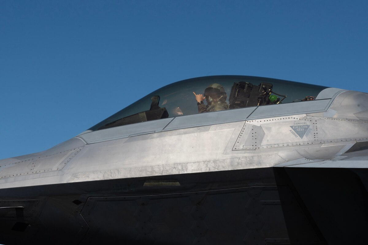A pilot holds up a hand signal from the cockpit of a military jet.