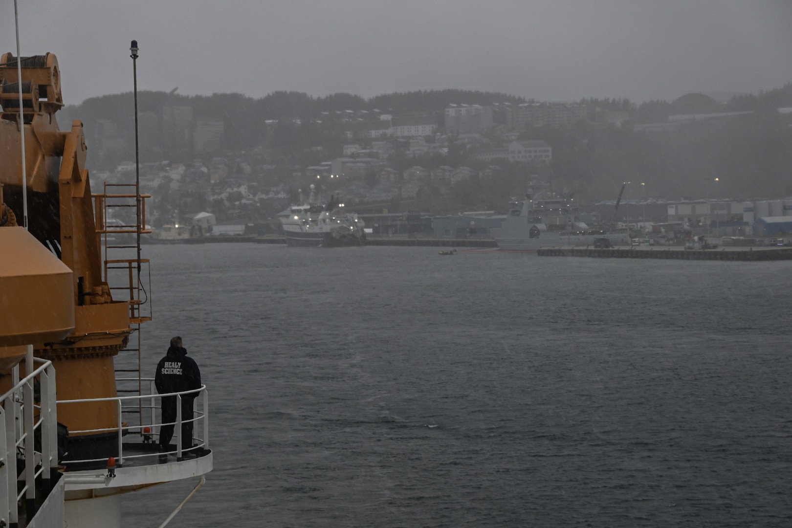 A U.S. Coast Guard Cutter Healy (WAGB 20) crew member looks at Tromsø, Norway as the cutter departs Tromsø, Oct. 5, 2023. During the four-day port call, the Healy and crew conducted joint operations with the Norwegian Coast Guard Vessel Svalbard, hosted a U.S. Coast Guard Research and Development Center (RDC) science roundtable, and welcomed aboard guests from a variety of institutions with interest in the Arctic and Healy’s science mission. (U.S. Coast Guard photo by Senior Chief Petty Officer Charly Tautfest)