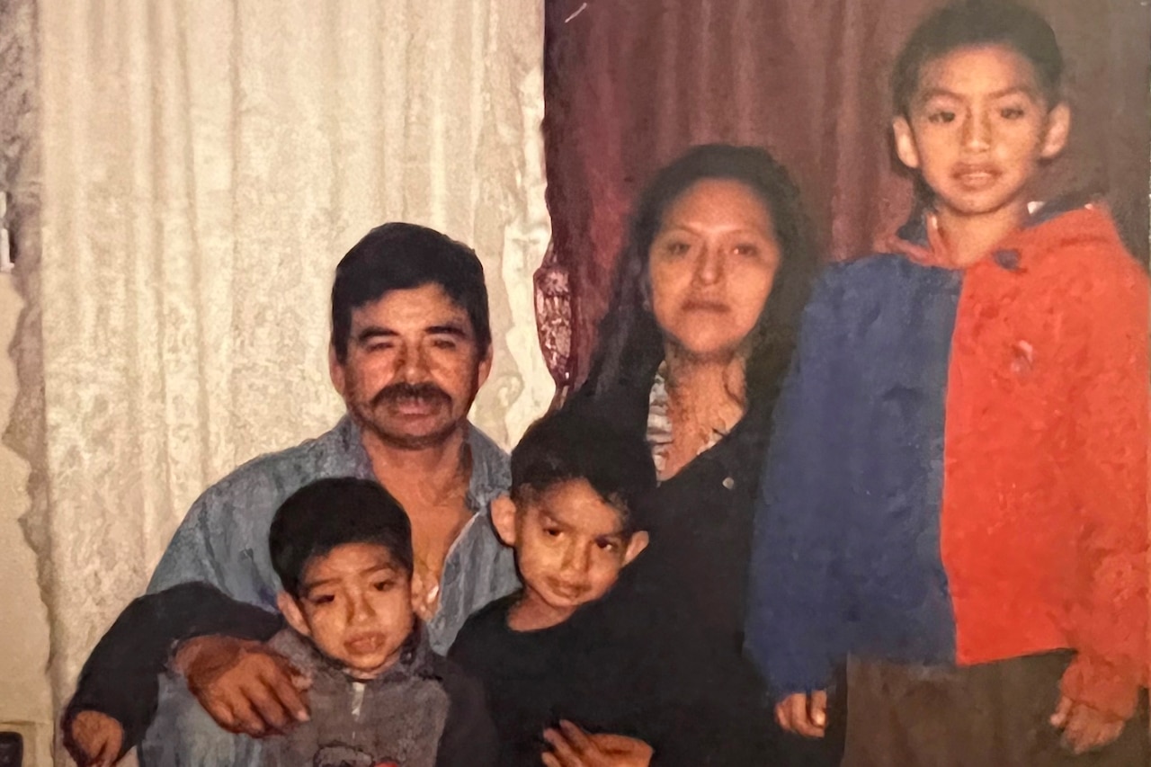 A young man and woman kneel as they pose for a photo with three little boys.