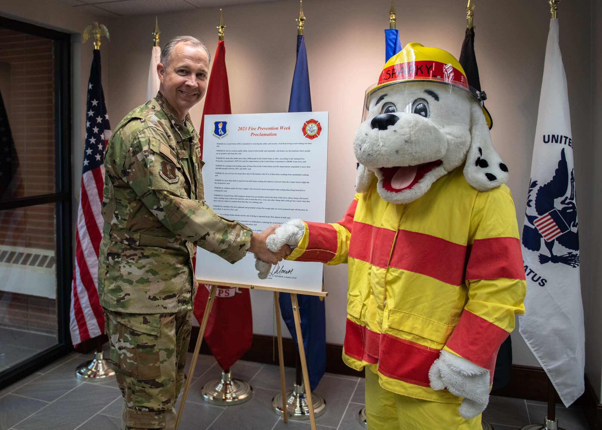 A man in a green uniform shakes hands for Sparky the fire dog