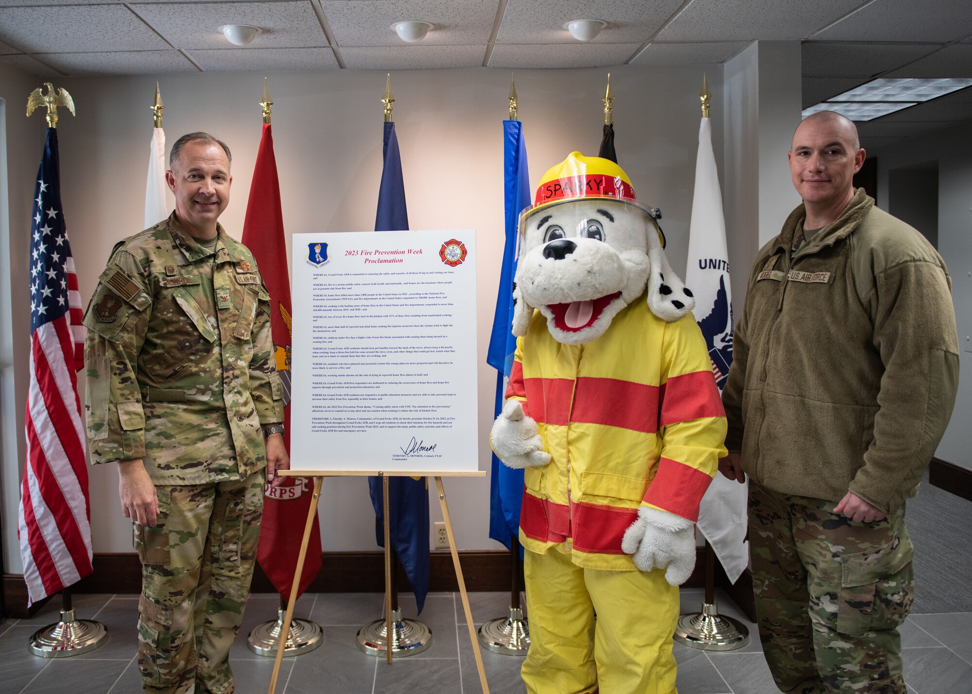 Two people in green uniforms and Sparky the fire dog pose for a photo.