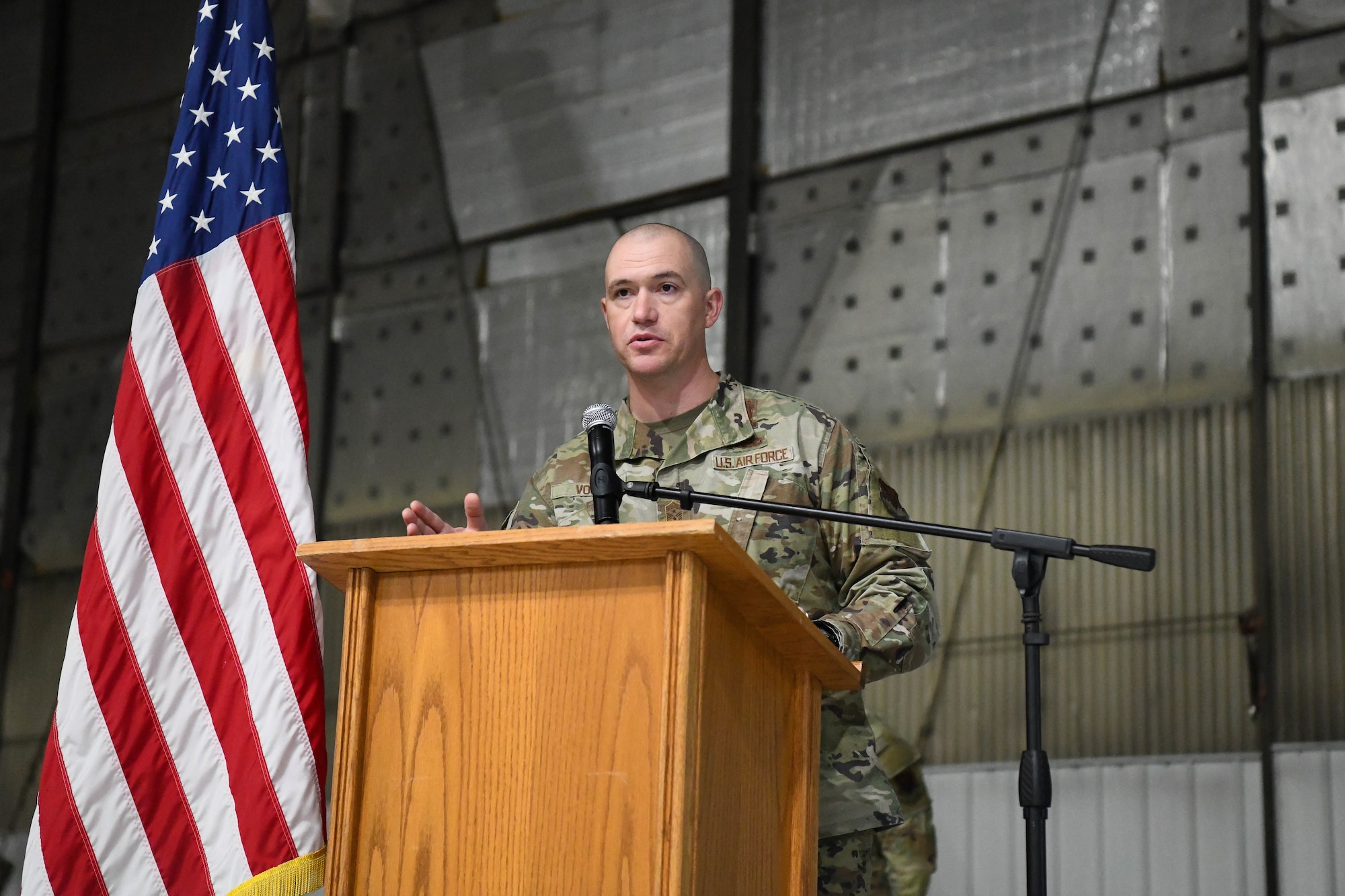 Man in military uniform talks at a podium next to an american flag.