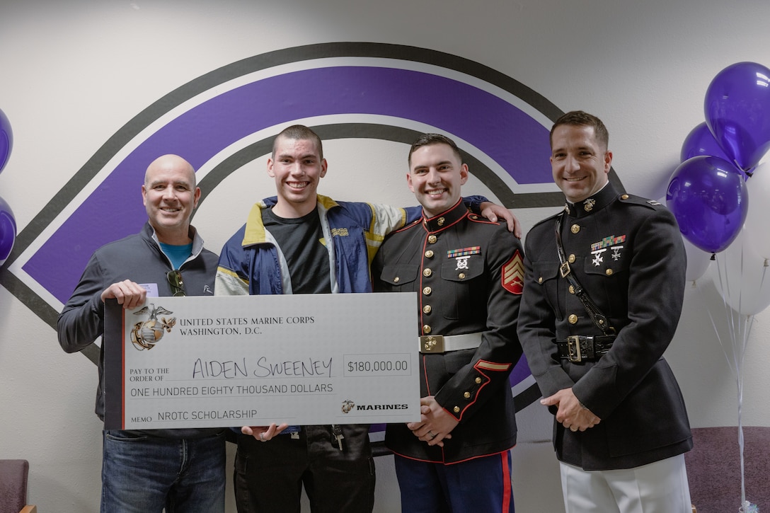 U.S. Marine recruiter and executive officer of Recruiting Station San Diego, pose for a photo of during a presentation of the Naval Reserve Officer Training Corps (NROTC) Scholarship to Aidan Sweeney and his father at Carlsbad High School in San Diego, California on March 30, 2023. Students selected for this prestigious scholarship program must uphold strict physical standards and successfully complete additional military courses while maintaining normal college coursework responsibilities. (U.S. Marine Corps Photo by Sgt. Ariana Lippert/Released)