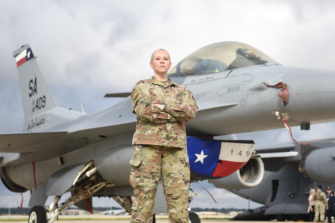 A woman in OCPs poses in front of an F-16.