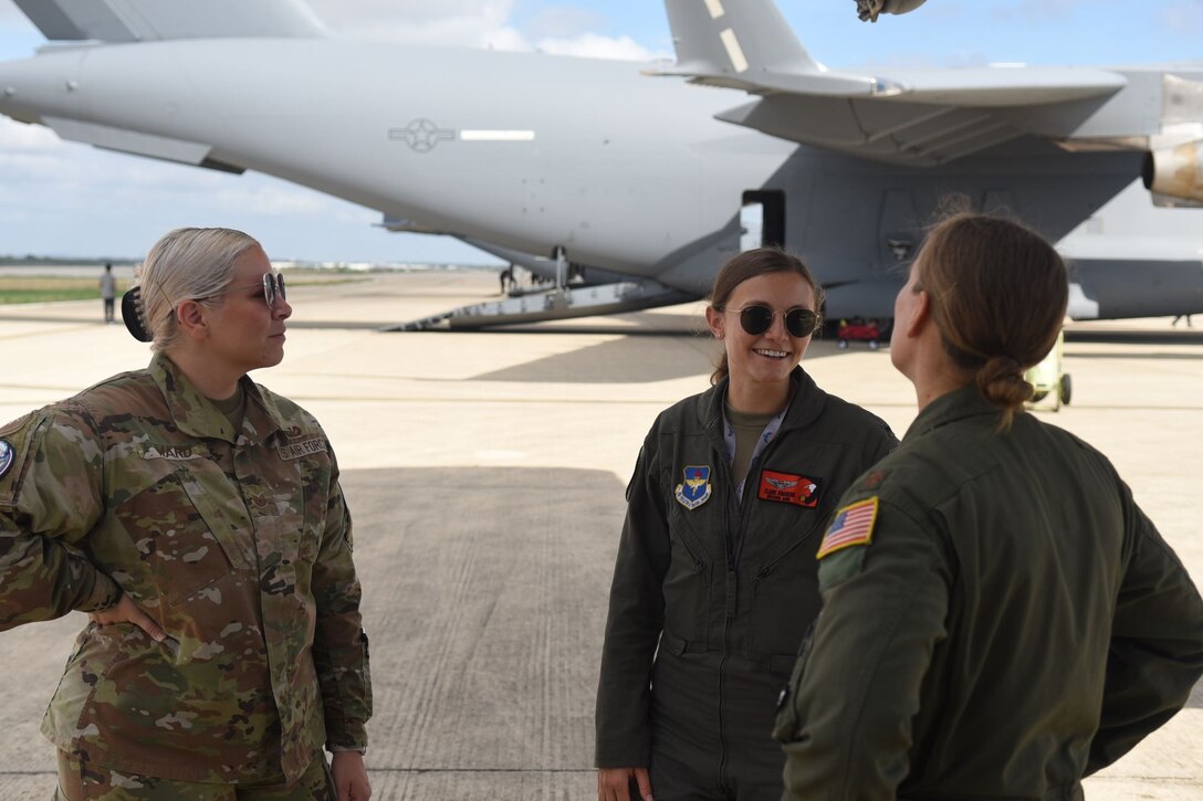 Two women in flight suits and another in OCPs engage in conversation with a C-17 in the background.