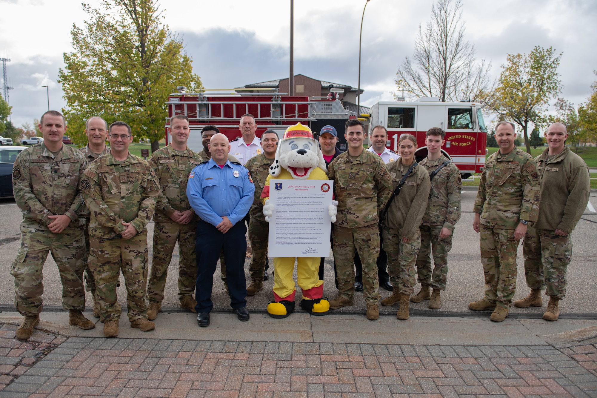 People in green uniforms and Sparky the fire dog pose for a group photos.