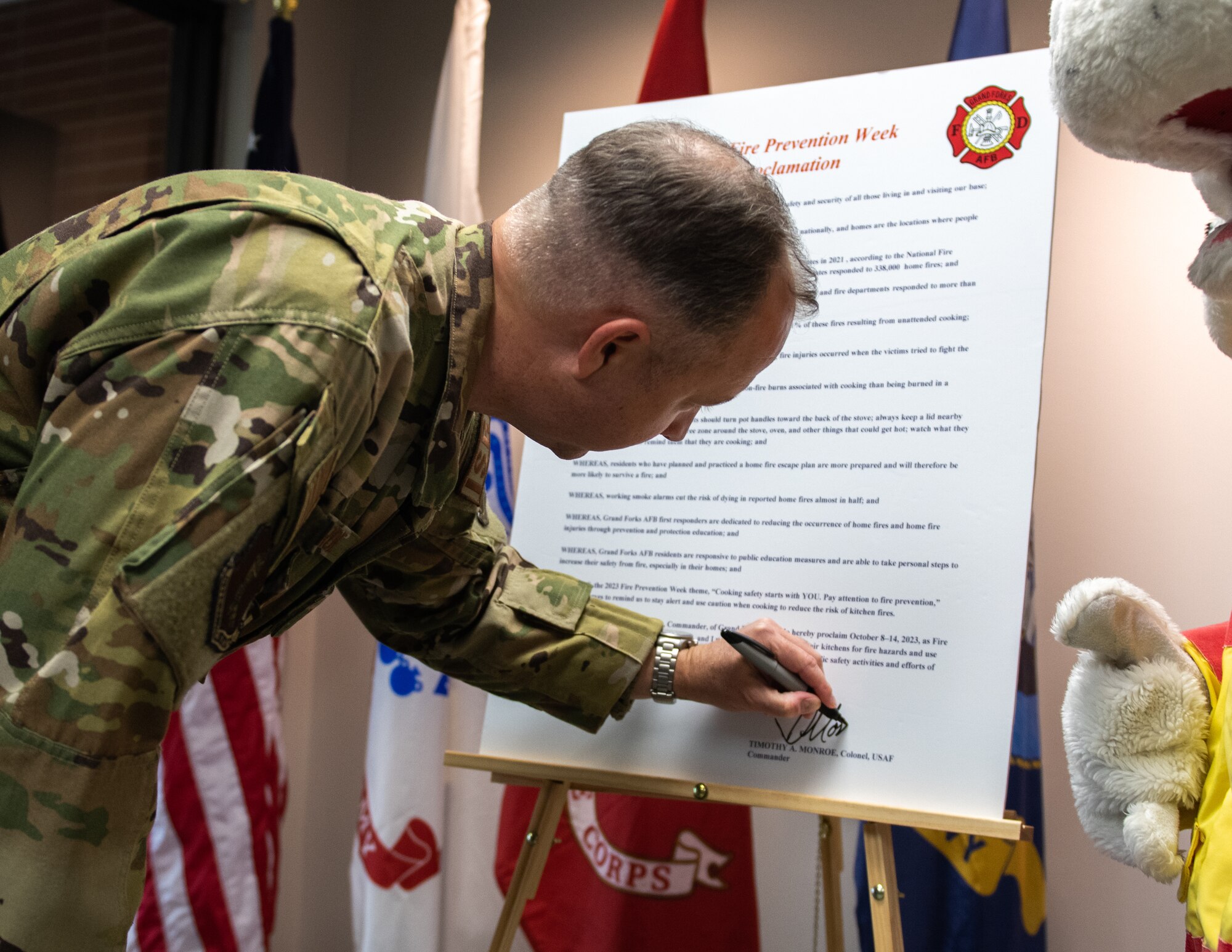 A man in a green uniform signs a large sheet of paper