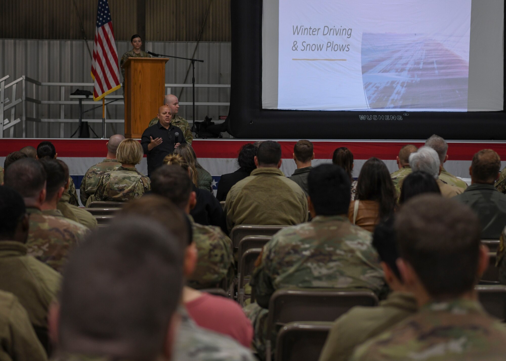 A man stands in front of a crowd and presents a slide show to them.
