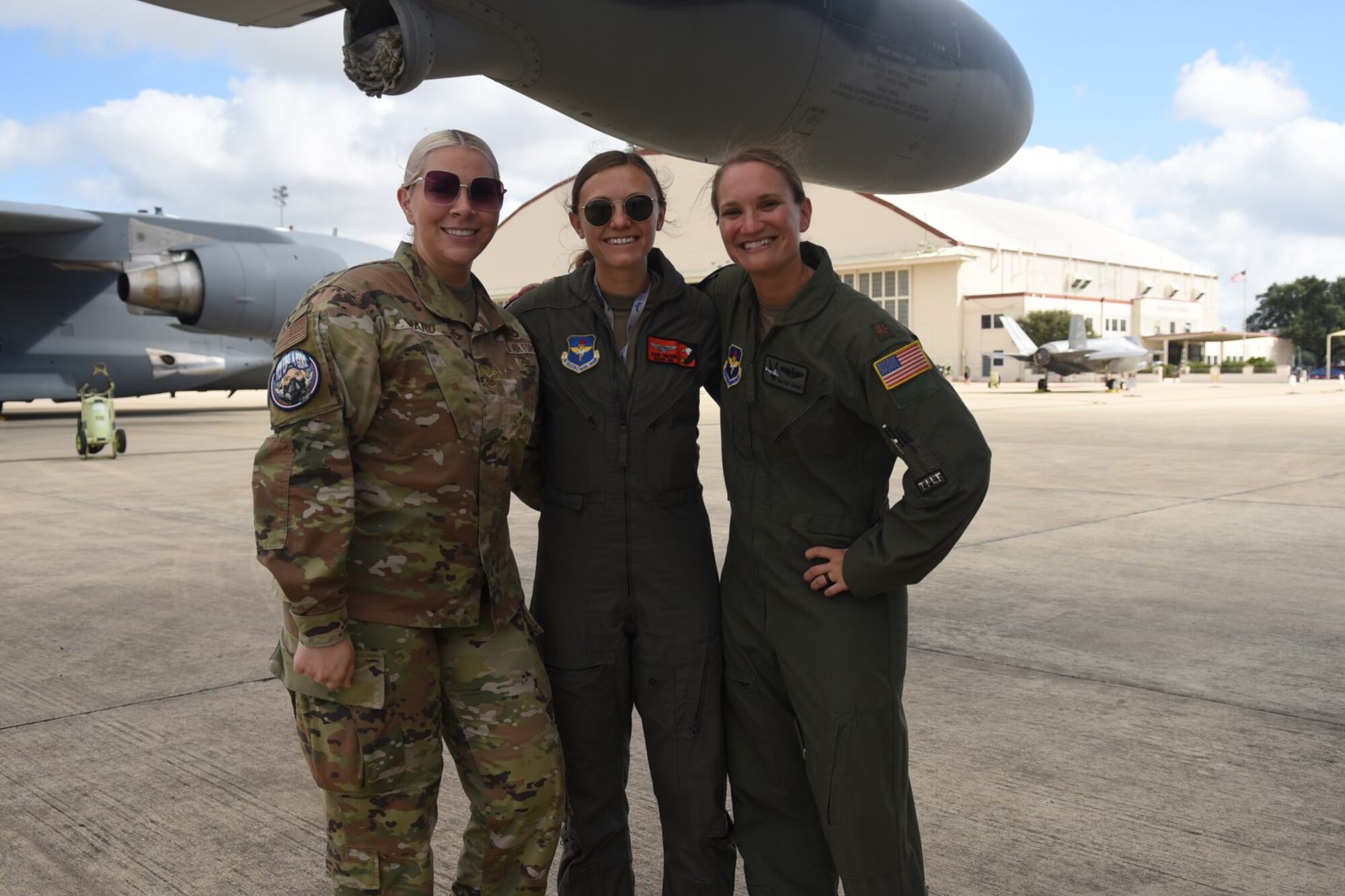 Two women in flight suits and another in OCPs pose under the wing of an aircraft.