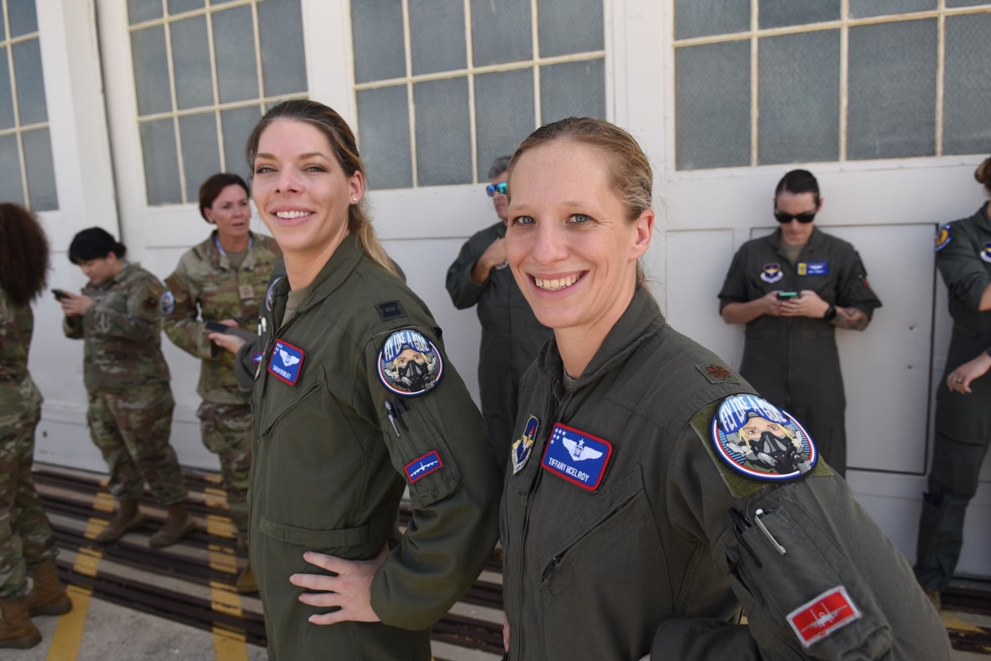Two women in flight suits pose together, showing off their "Fly Like a Girl" patches.