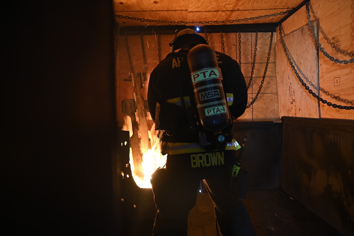 Airmen firefighters enter a burning building to put out a fire.