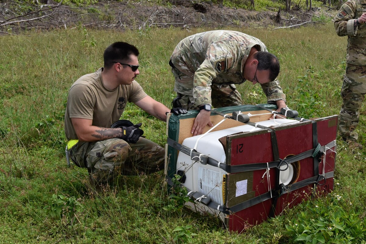 Two Airmen collect the Low Cost, Low Altitude bundles after the drop from an aircraft.