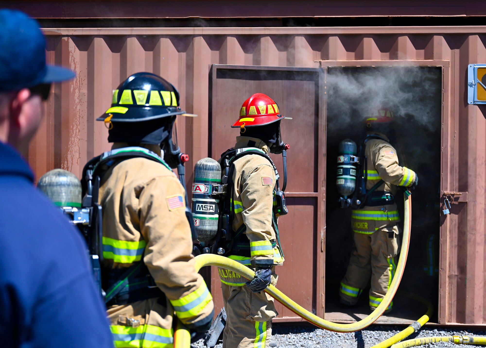 Airmen firefighters enter a burning building to put out a fire.