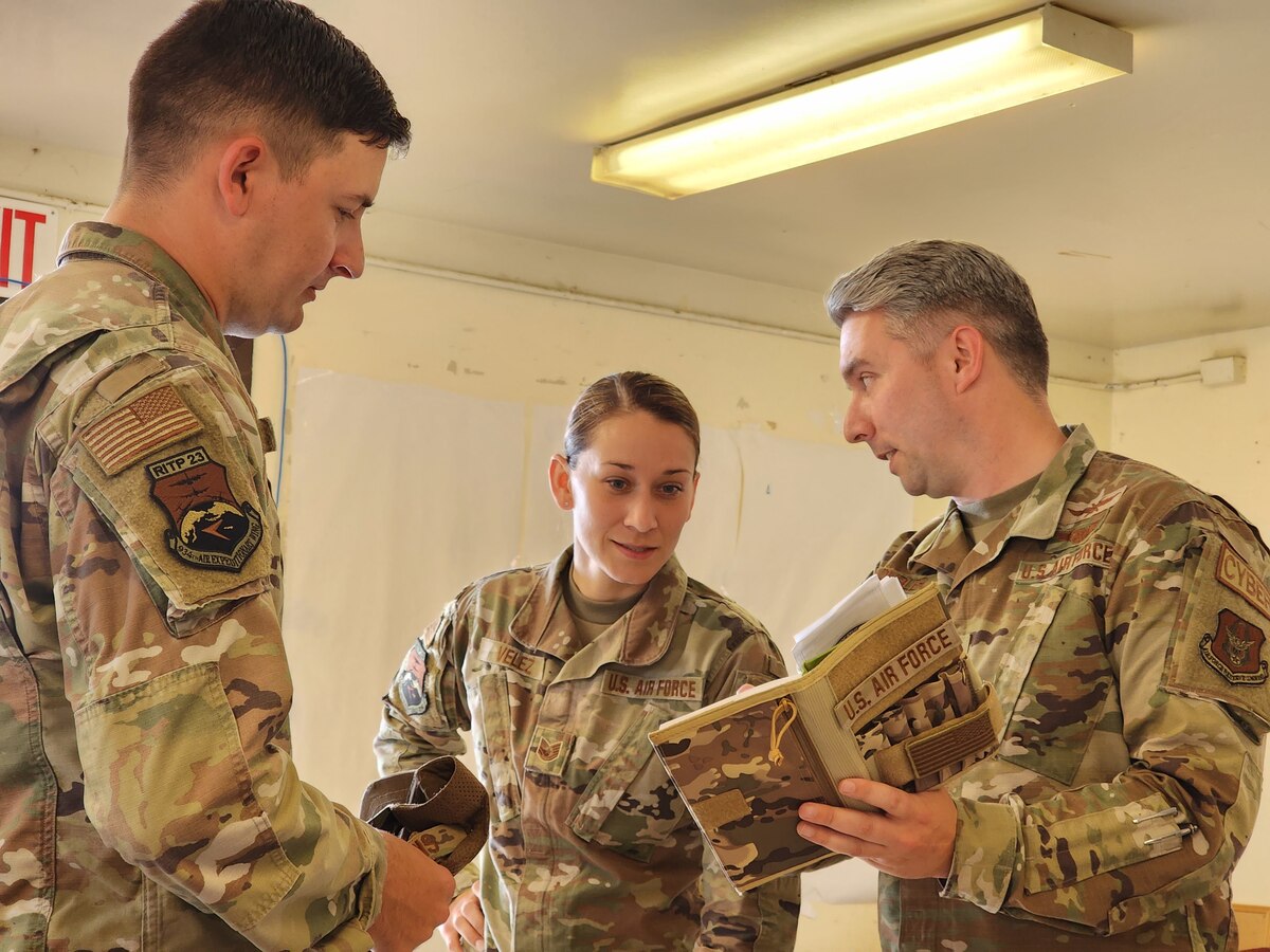 Three Airmen stand together talking and looking at some paperwork.