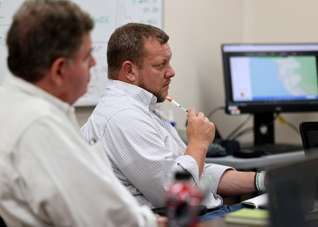 Two men sit in an office setting listening to a meeting.