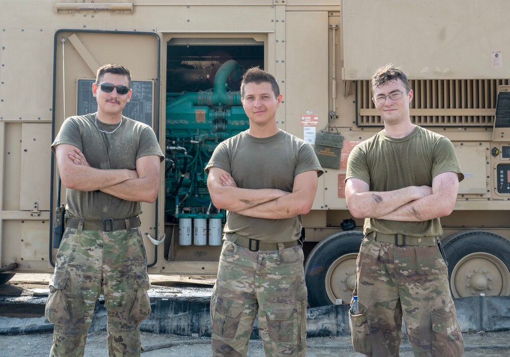 A photo of three Airmen standing in front of a generator.