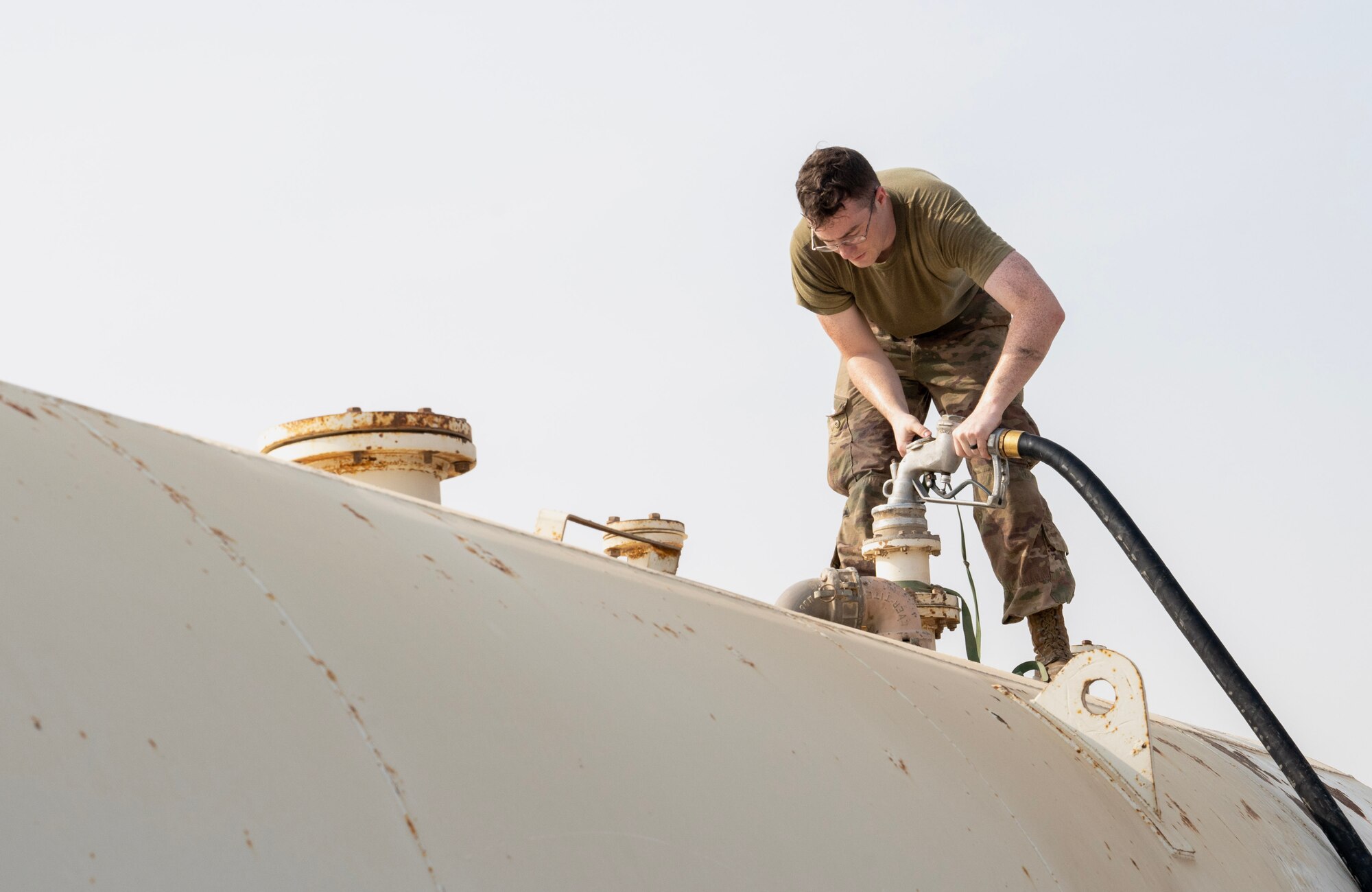 A photo of an Airman standing on top of a fuel tank, filling it with a hose.