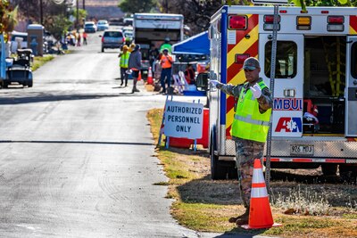 A man in military uniform is seated at the head of a table surrounded by men and women in uniform and civilian attire.