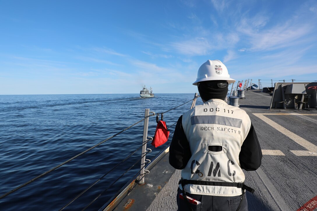 A senior officer stands on the deck of a ship at sea.