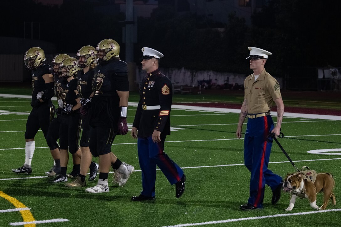 U.S. Marine Corps Pfc. Bruno, the mascot for Marine Corps Recruit Depot San Diego, and his handler, Sgt. Tyler Abbott, a combat graphic specialist at MCRD, participate in the coin flip ceremony for the Point Loma High School football game in San Diego, Oct. 5, 2023. The mascot's job is to boost morale, participate in outreach work, and attend events and ceremonies. (U.S. Marine Corps photo by Lance Cpl. Jacob B. Hutchinson)