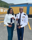 Man on the right in an Army uniform, holding a customized tie and a woman on the left in a white blouse and teal pants holding a similar customized tie