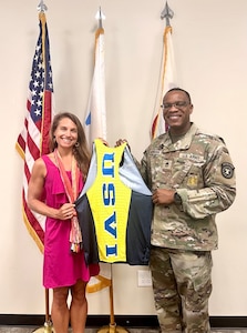 Man standing on the right in an Army uniform and woman standing on the left in a pink dress hold a USVI jersey.