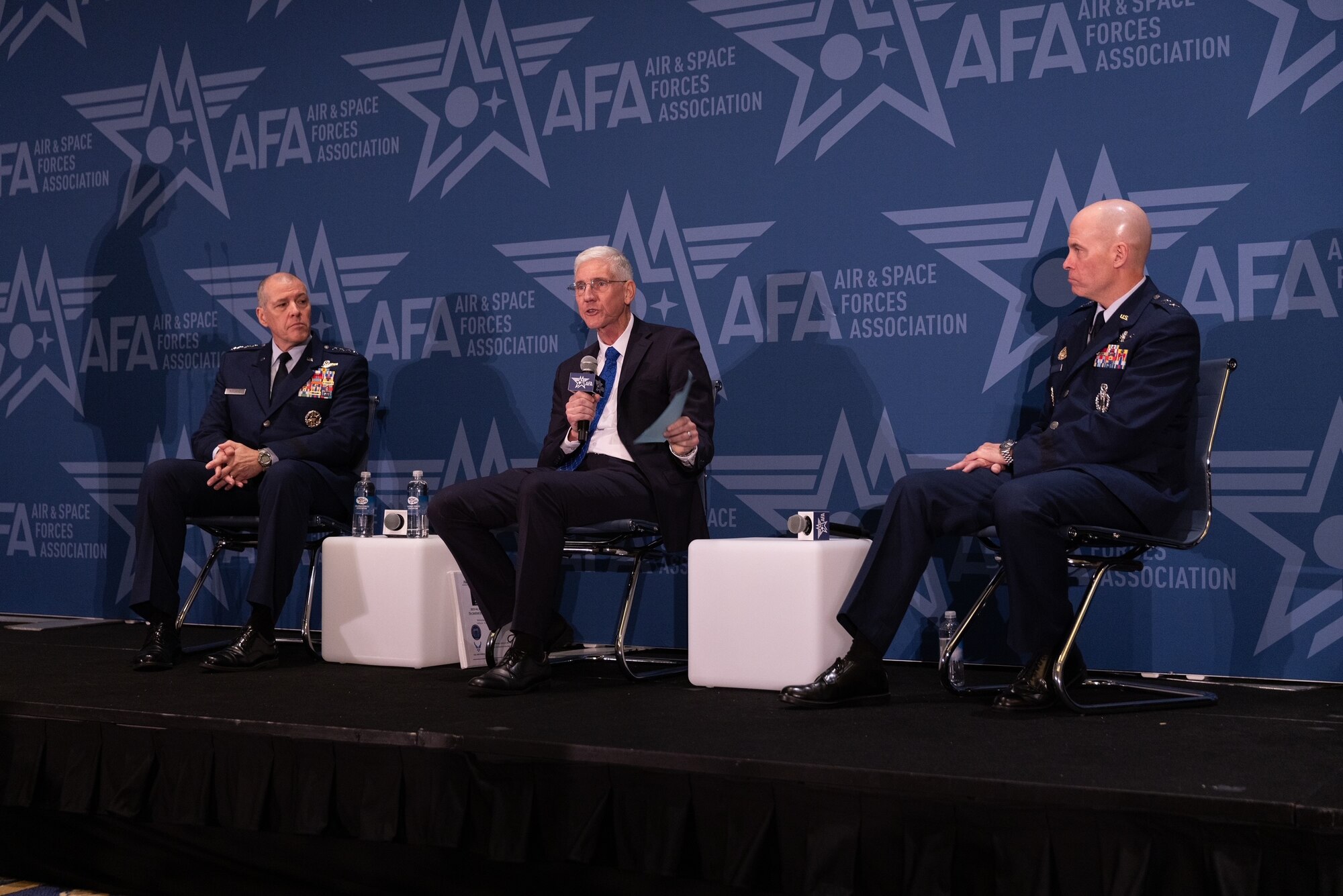 Three people sit on a stage and talk during a conference.