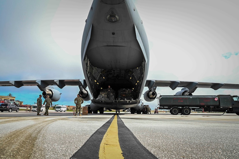 Service members in uniform stand near a military cargo plane.