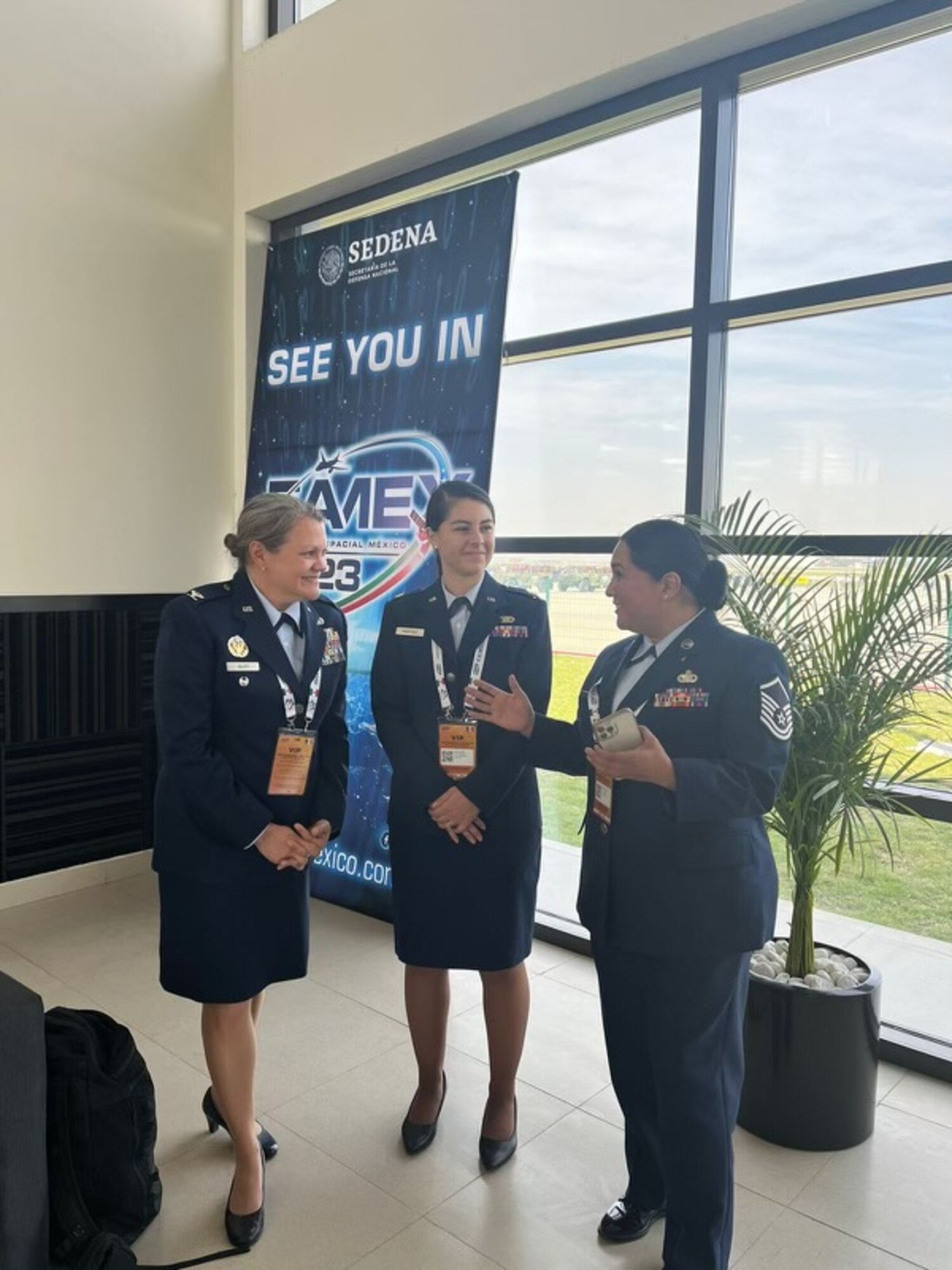 Three women in U.S. Air Force service dress converse while standing in a room.