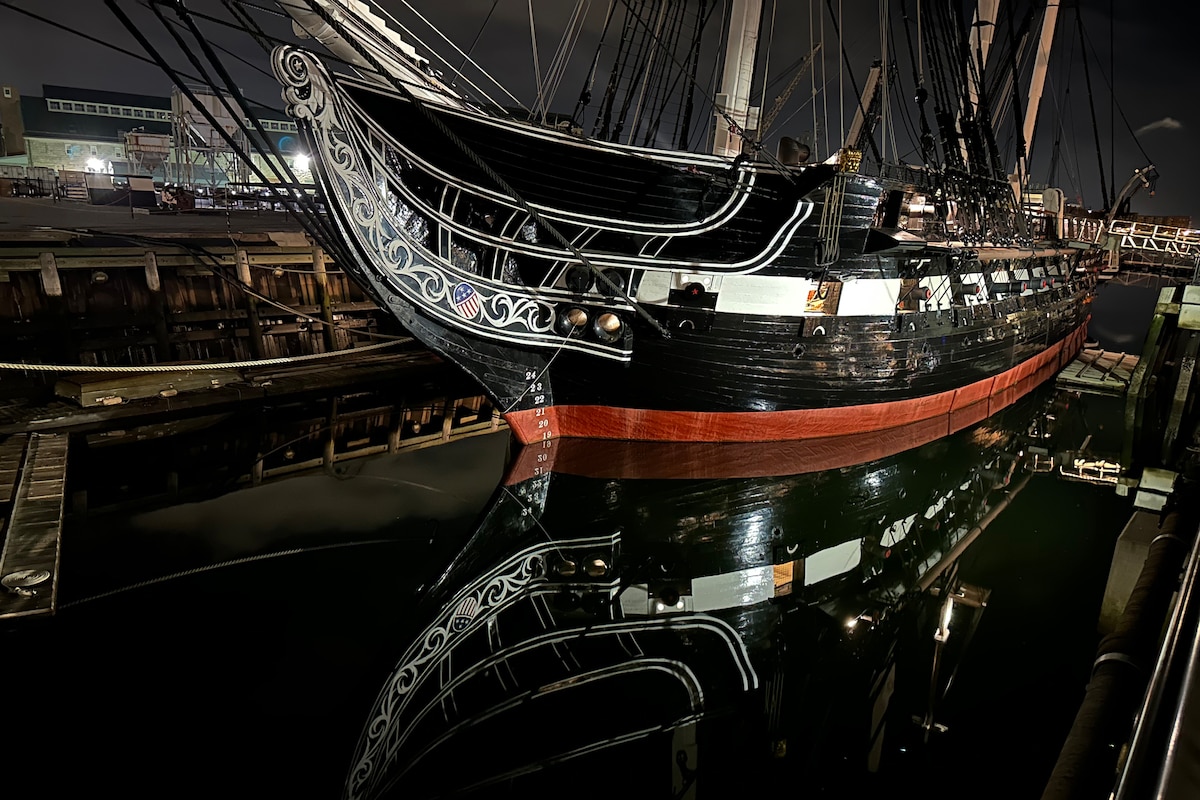 An old ship’s reflection is shown in a harbor at night.
