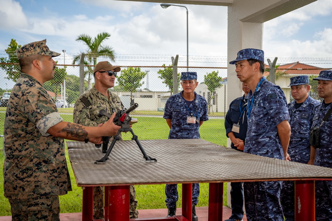Gunnery Sgt. Prince Bustos, left, assigned to Naval Mobile Construction Battalion (NMCB) 3, discusses the M240B machine gun to Japan Maritime Self-Defense Force (JMSDF) Capt. Hiromitsu Yuasa, right, and members of the JMSDF Engineering Group during a tour to showcase the capabilities of the Naval Construction Force onboard Camp Shields, Okinawa, September 7th.