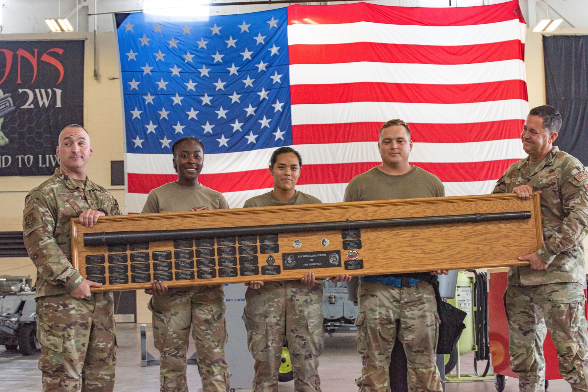 Five Airmen from hold a plaque with winning names for quarterly and annual load competitions.