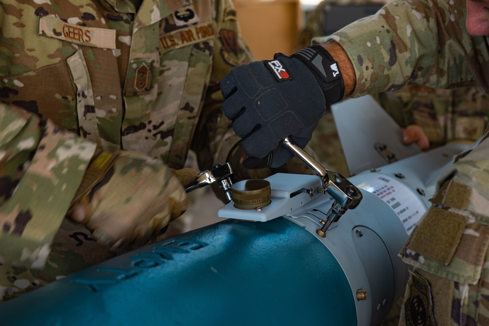 One Airman holds down metal while another uses a tool to tighten screws.