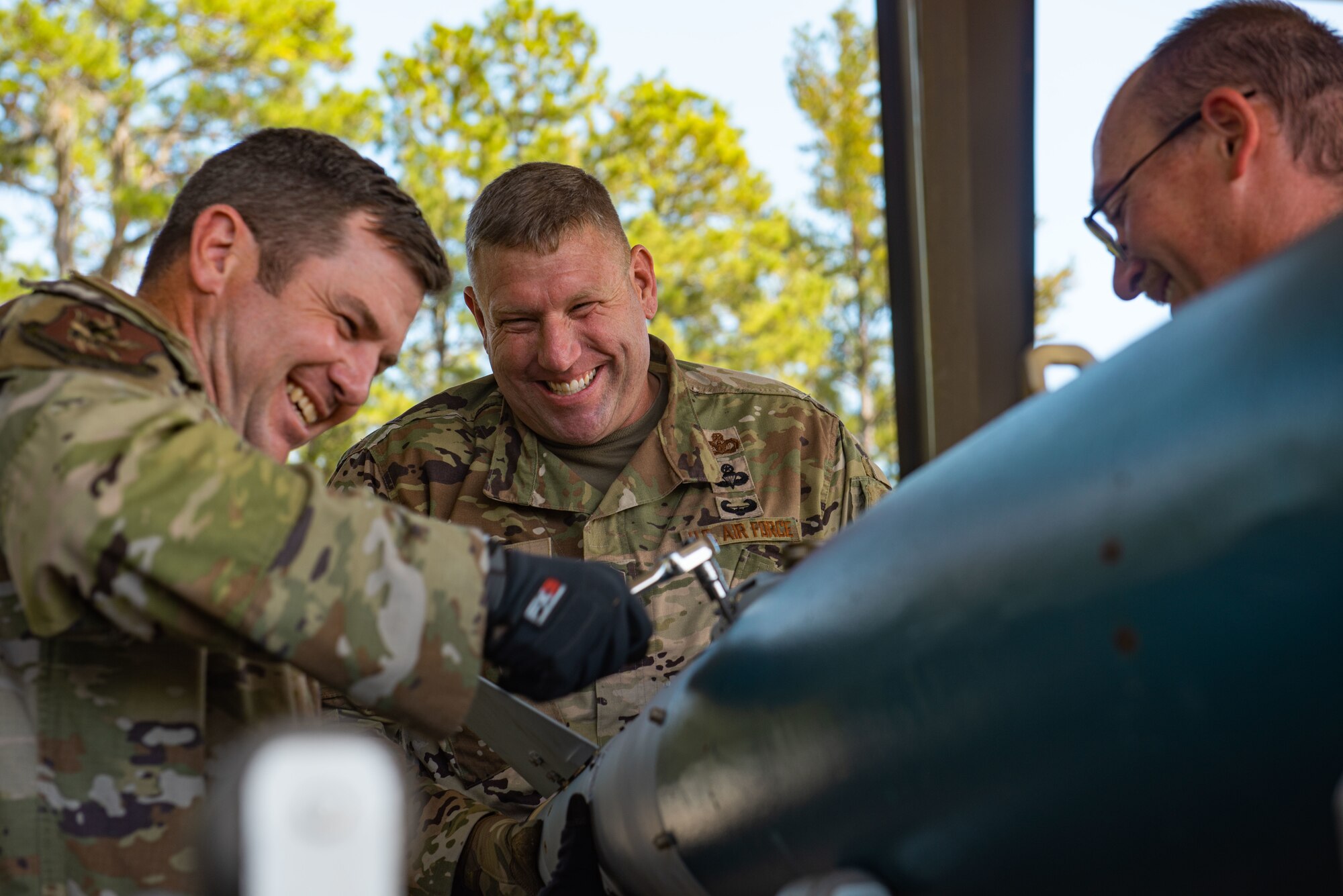 Three people surround an item being wrenched.