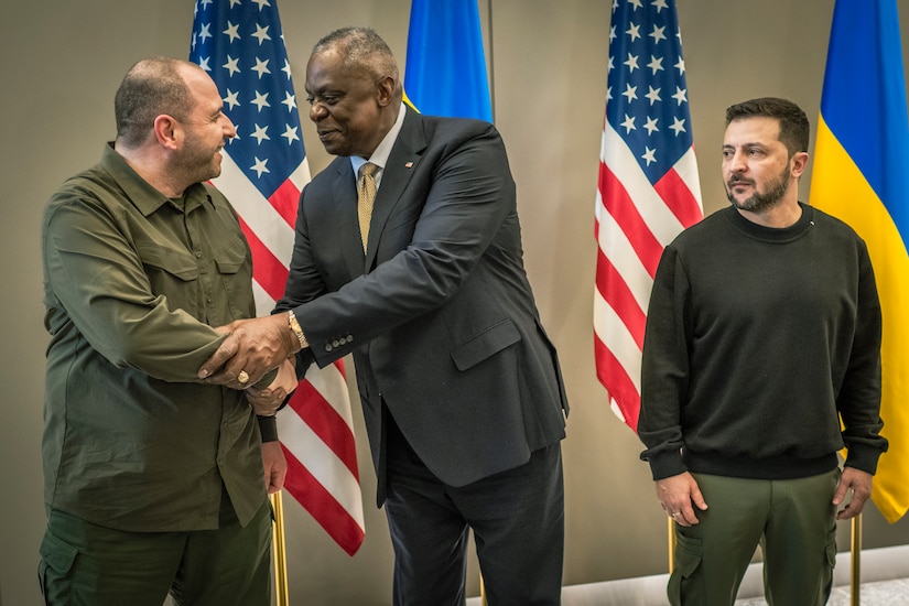 Two men shake hands; U.S. and Ukranian flags are in the background.