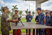 Gunnery Sgt. Prince Bustos, left, assigned to Naval Mobile Construction Battalion (NMCB) 3, discusses the M240B machine gun to Japan Maritime Self-Defense Force (JMSDF) Capt. Hiromitsu Yuasa, right, and members of the JMSDF Engineering Group during a tour to showcase the capabilities of the Naval Construction Force onboard Camp Shields, Okinawa, September 7th.