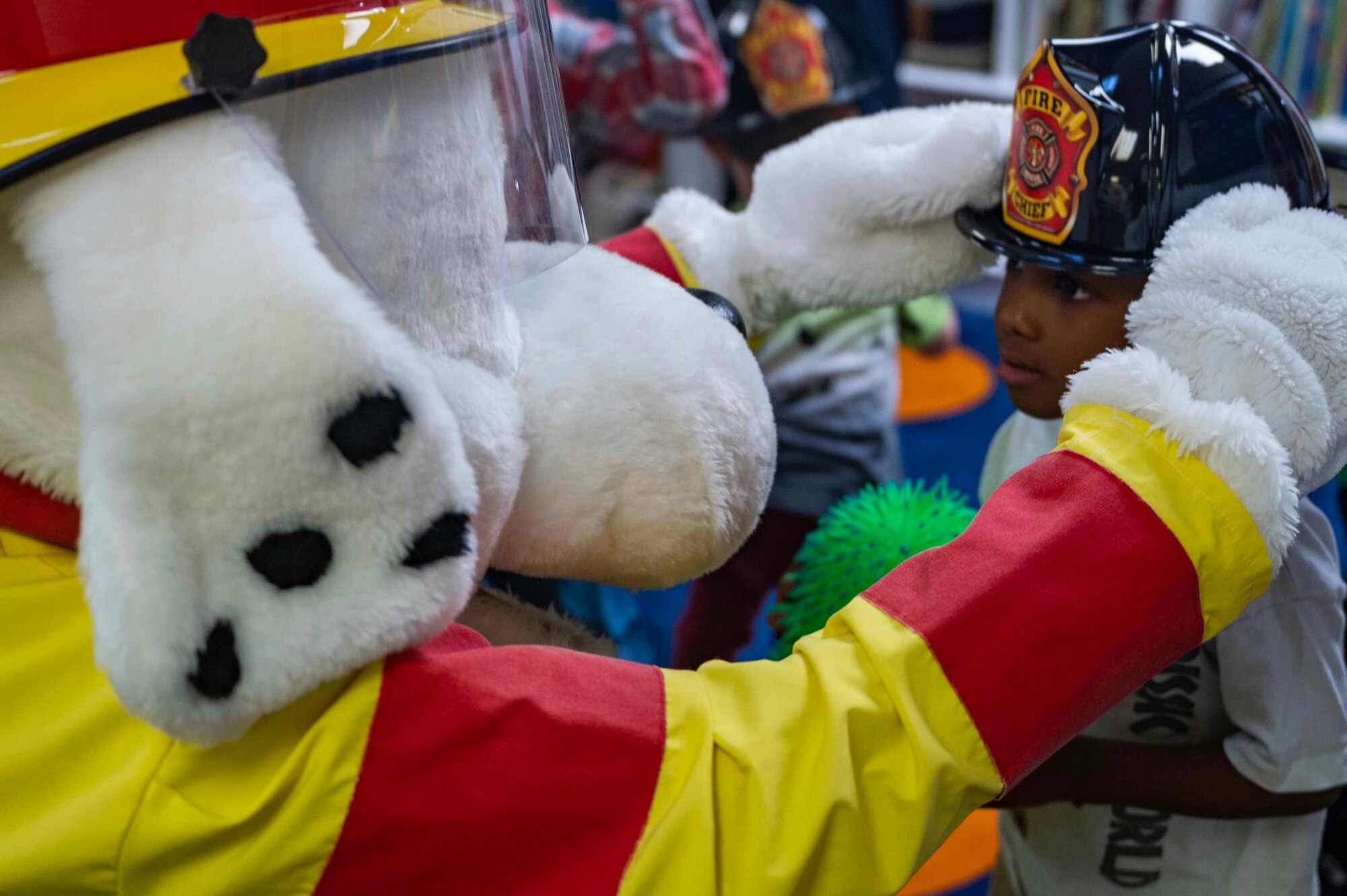 Sparky the Fire Dog gives out fire helmets during a visit by the 100th Civil Engineer Squadron Fire Department to the 100th Force Support Squadron Child Development Center at Royal Air Force Mildenhall, England, Oct. 11, 2023. Sparky the Fire Dog is a Dalmatian who has been the official mascot of National Fire Protection Association, a U.S. organization in charge of creating and maintaining minimum standards and requirements for fire prevention, suppression training, and equipment since 1951. (U.S. Air Force photo by Senior Airman Viviam Chiu)
