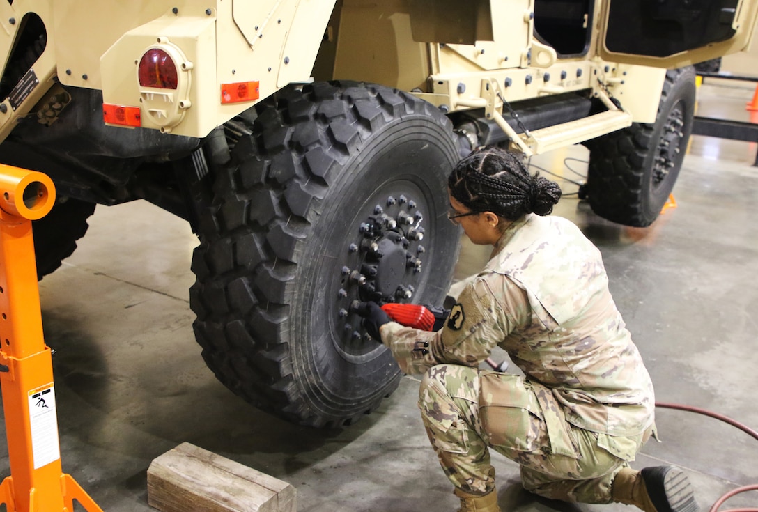 A soldier uses a tool to secure lug nuts on a military vehicle’s tire.