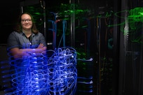 Woman engineer stands in front of blue IT lights.