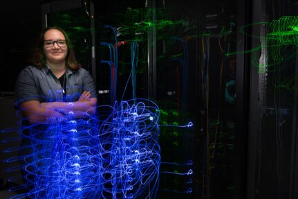Woman engineer stands in front of blue IT lights.
