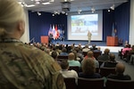 an auditorium full of people and two speakers on the stage