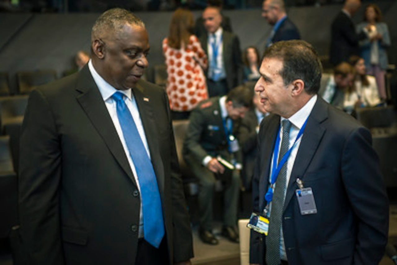 Two men talk while people mill about in the background.