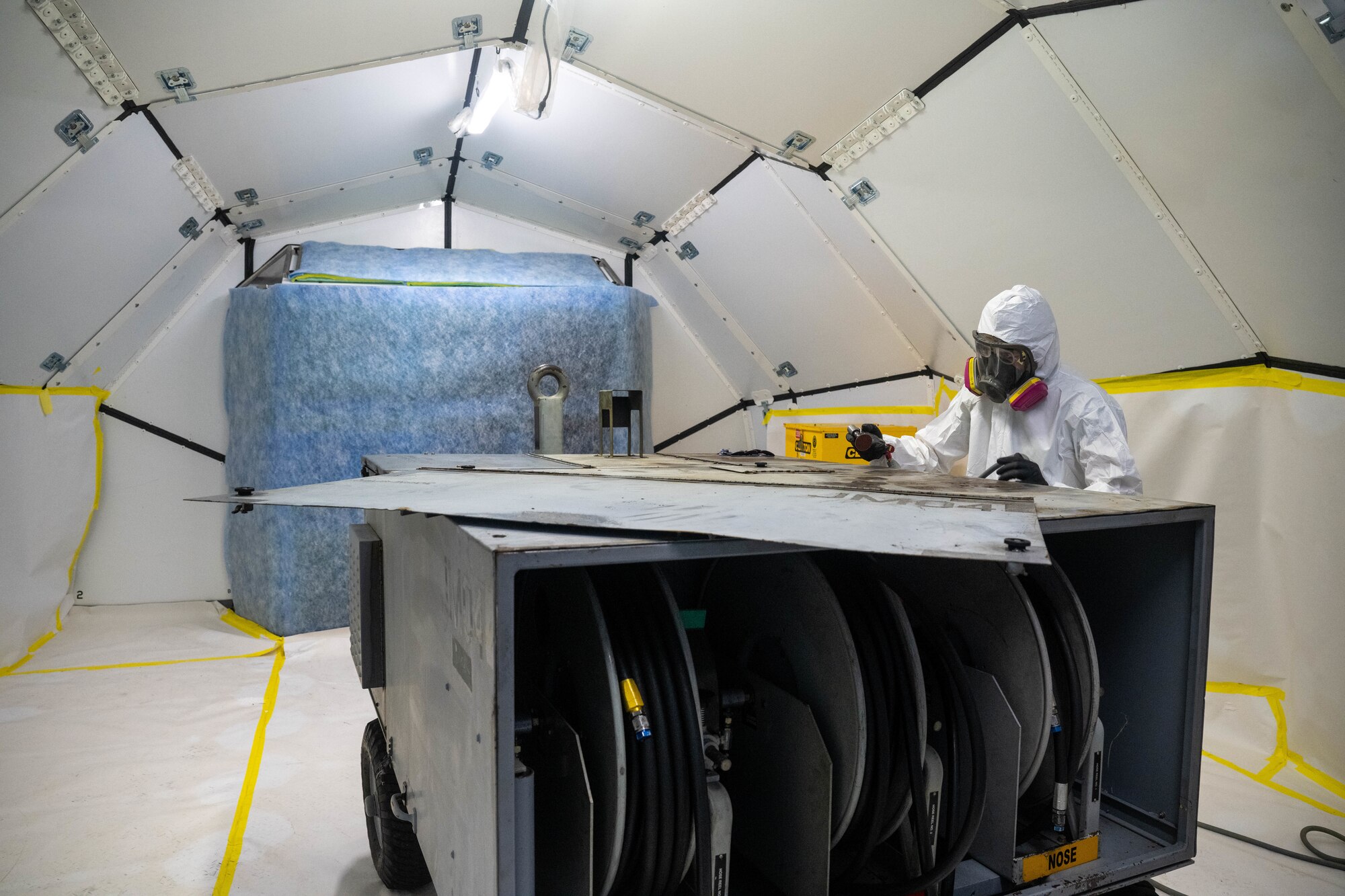 Airman 1st Class Tyler Edwards, 15th Maintenance Squadron aircraft structural maintenance journeyman, sands a corroded hydraulic cart in preparation for repair in a new mobile paint booth at Joint Base Pearl Harbor-Hickam, Hawaii, Oct. 11, 2023. The mobile paint booth’s capabilities are currently being tested before it is approved for use in forward operating base environments.  (U.S. Air Force photo by Senior Airman Makensie Cooper)
