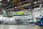 A Fleet Readiness Center Southeast (FRCSE) weight and handling crewmember helps to stabilize an F/A-18 Hornet as it is repositioned using a crane as part of a Center Barrel Replacement (CBR) maintenance evolution. CBRs were conducted to extend the service life of F-18A-D aircraft – saving the U.S. government millions in replacement costs. (U.S. Navy Photo by Toiete Jackson/Released)