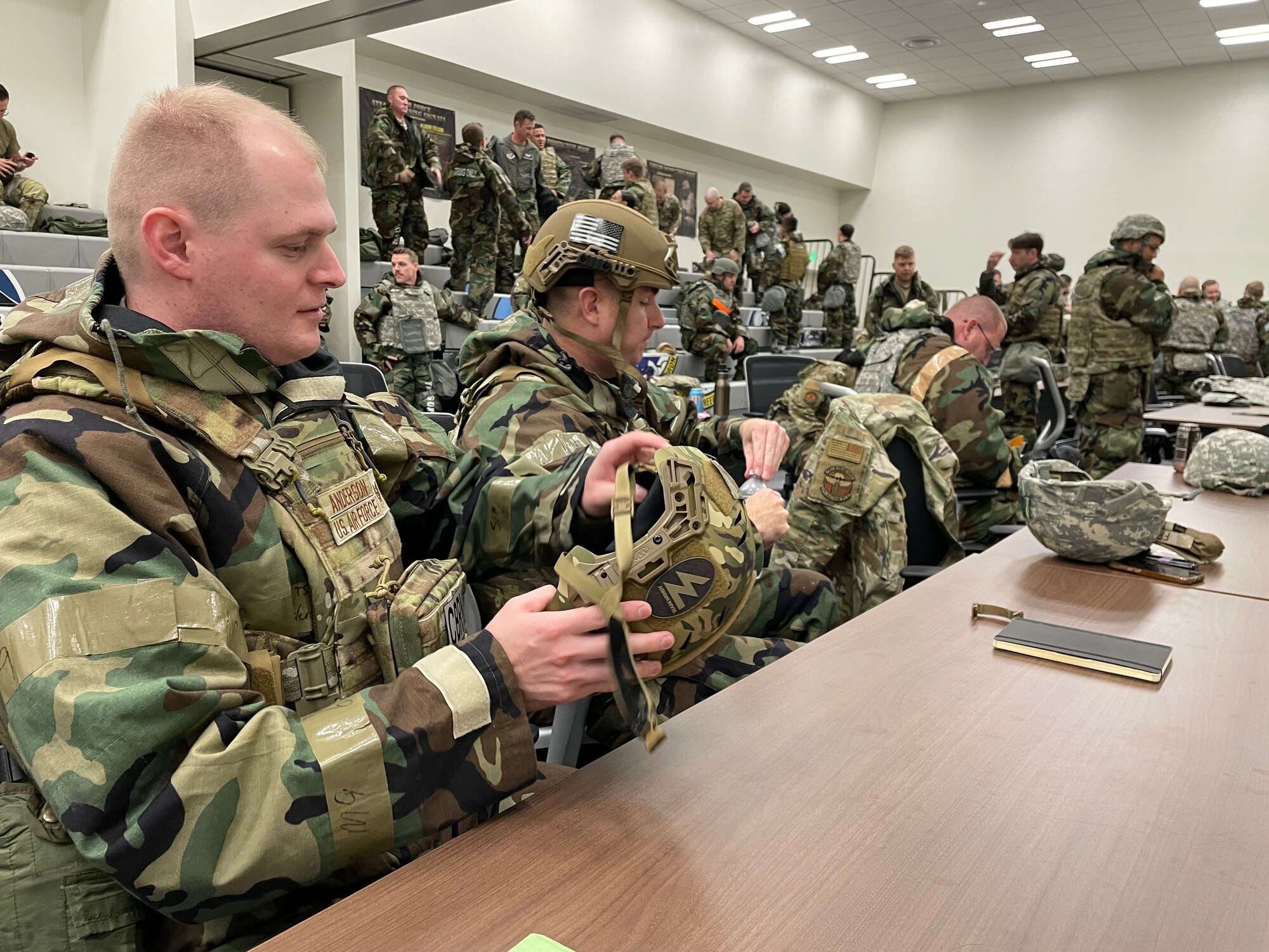 Dozens of soldiers work on dressing in protective gear in a conference room