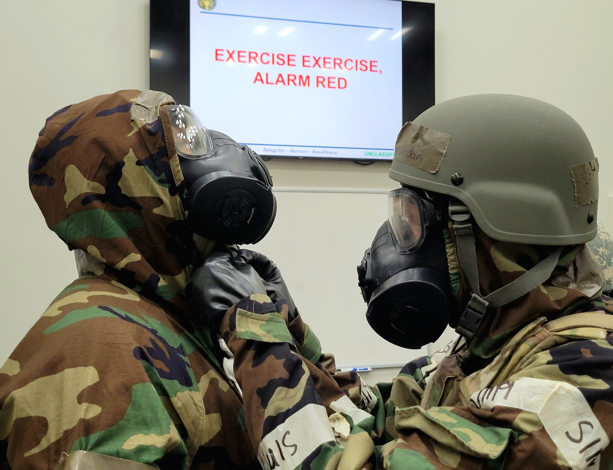 two soldiers clad in protective gear check over each other