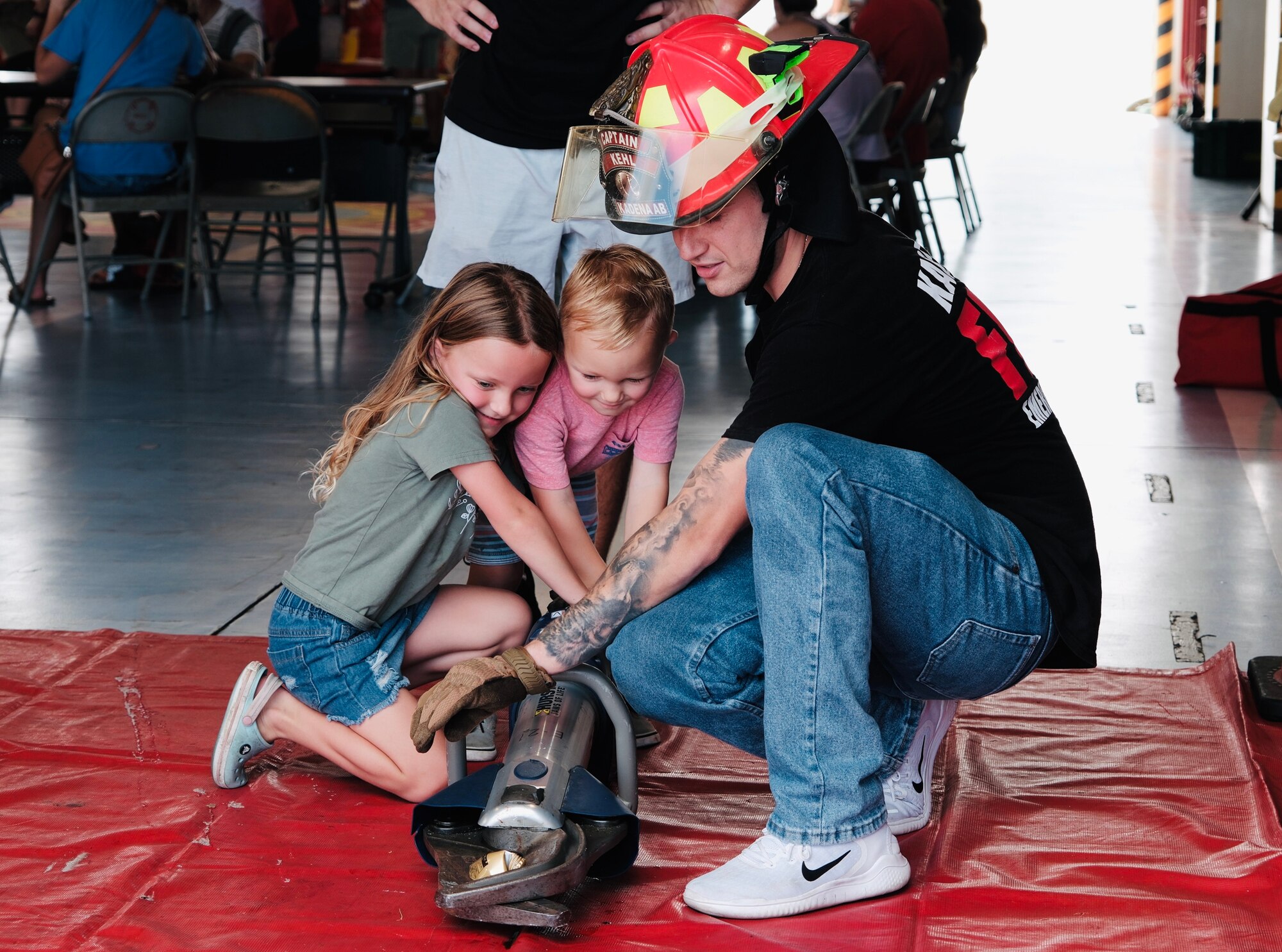 Firefighter helps two children handle firefighter equipment