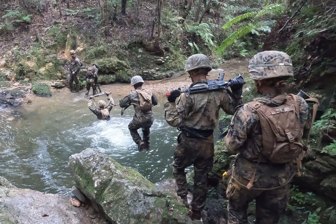 A group of Marines prepare to jump in a stream in a wooded area.