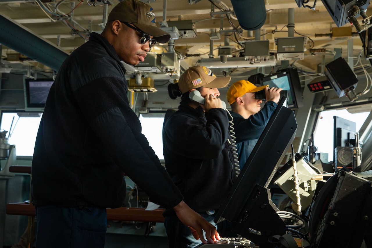 Sailors in uniform stand watch on the bridge of a Navy warship.