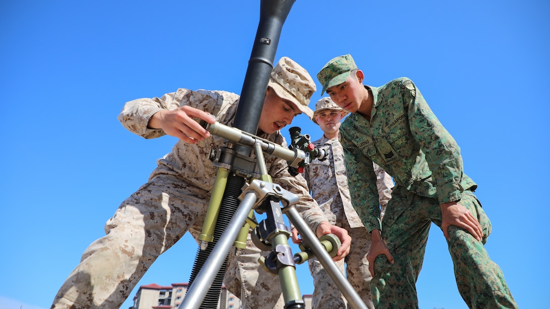 U.S. Marine Corps Lance Cpl. Gabriel Correia, left, Cpl. John T. Plunkett, center, mortarmen with 2nd Battalion, 4th Marine Regiment, 1st Marine Division, and Singapore Guardsmen 3SG Matthew Leong, a detachment commander with the 7th Singapore Infantry Brigade, conduct drills using a M252A2 81mm mortar system during a mortar subject matter expert exchange as part of Exercise Valiant Mark 2023 at Camp Pendleton, CA, Oct. 9, 2023. Valiant Mark 2023 is an annual, bilateral training exercise conducted between the Singapore Armed Forces and I Marine Expeditionary Force, designed to enhance interoperability, improve combined arms and amphibious warfighting skills, and strengthen military-to-military relationships. (U.S. Marine Corps photo by Sgt. Quince D. Bisard)